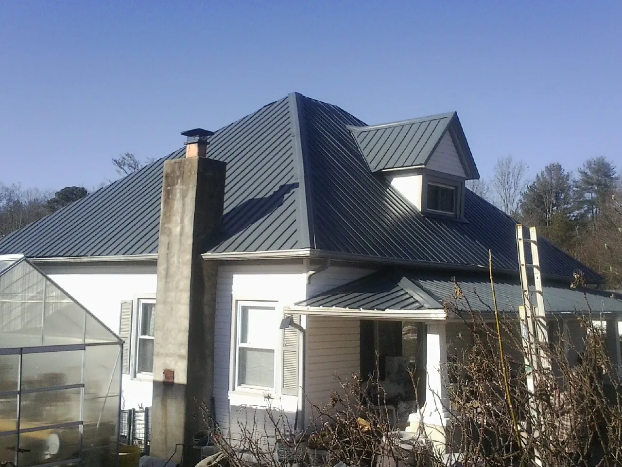Dark blue standing seam metal roof on a white farmhouse with dormer — Slate & Tile Roof Repair by Roofing Brothers in Sedley