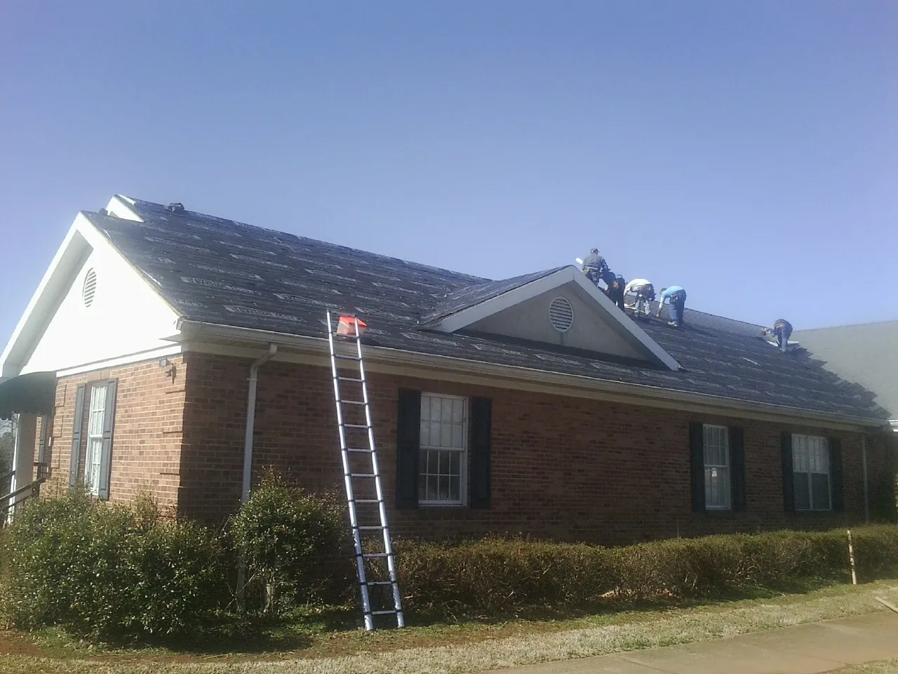 Crew tearing shingles off a brick ranch roof with a ladder set — Metal Roof Repair work by our crew in Sedley