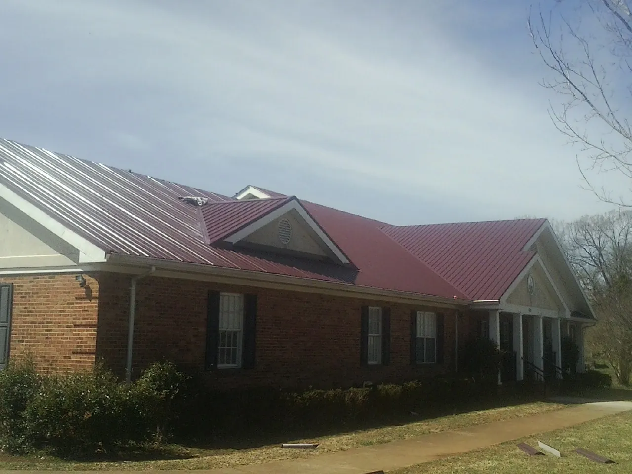 Red metal roof with gabled entries on a long brick building, from a Hail Damage Roof Repair job in Sedley