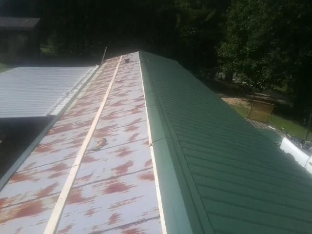 Old rusted panels beside newly installed green metal roofing — Wind Damage Roof Repair by Roofing Brothers in Sedley