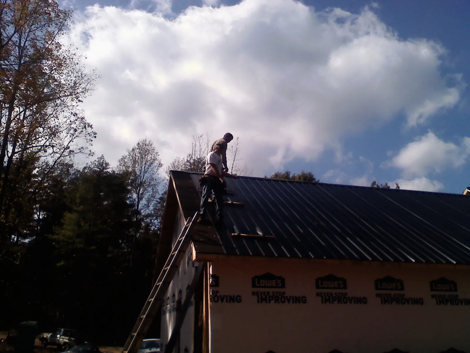 Roofer fastening dark metal panels high against a cloudy sky, from a Roof Inspection job in Sedley