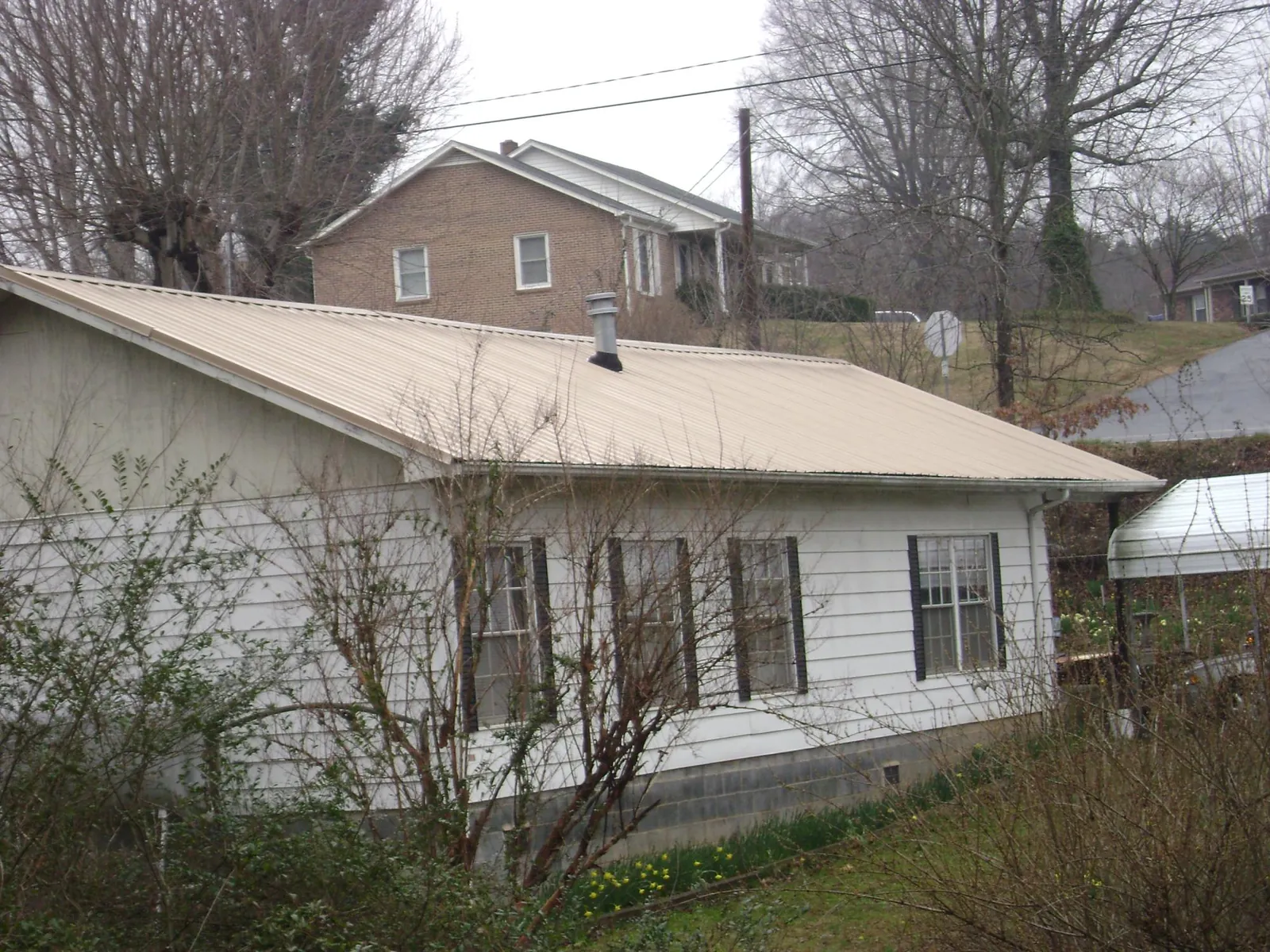 Tan metal roof on a white sided house set into a hillside — Commercial Roofing by Roofing Brothers in Sedley