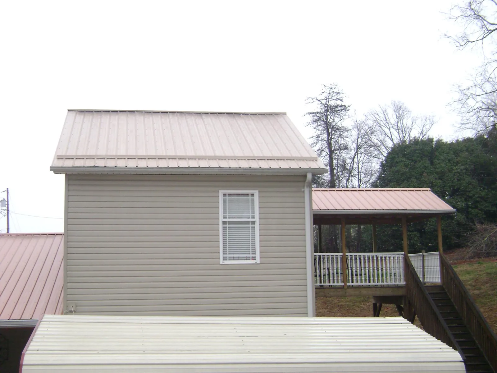 Tan metal roofs on a two story addition and attached porch, from a Roof Replacement job in Sedley